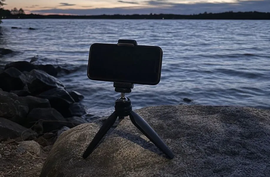 A phone on a small tripod mount by a lakeshore after sunset in blue evening light