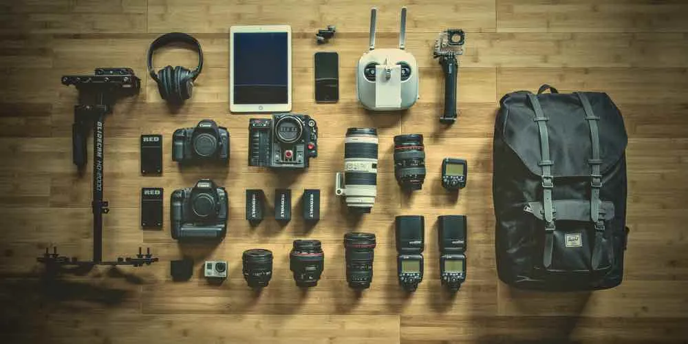 Camera gear, a tablet and a backpack laid out on a wooden floor