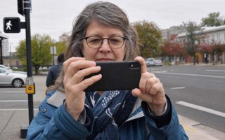 Front close view of an everyday person holding a phone up to frame a street scene