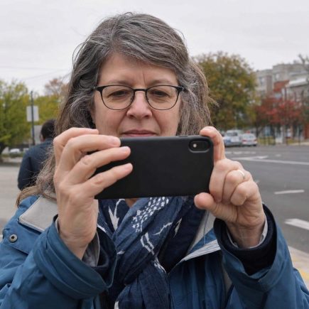 Front close view of an everyday person holding a phone up to frame a street scene