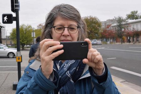 Front close view of an everyday person holding a phone up to frame a street scene