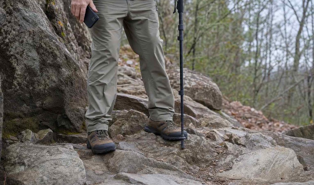 Sturdy walking shoes planted on an uneven rocky trail, a phone held lowered at the walker's side