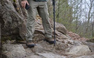 Sturdy walking shoes planted on an uneven rocky trail, a phone held lowered at the walker's side