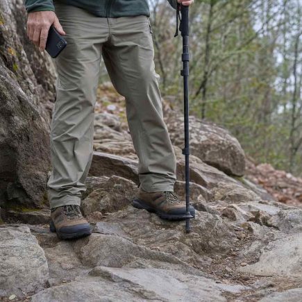 Sturdy walking shoes planted on an uneven rocky trail, a phone held lowered at the walker's side