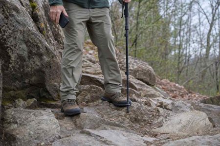 Sturdy walking shoes planted on an uneven rocky trail, a phone held lowered at the walker's side
