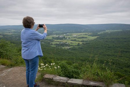 Side view of a person at a hillside overlook holding up a phone to a broad green valley