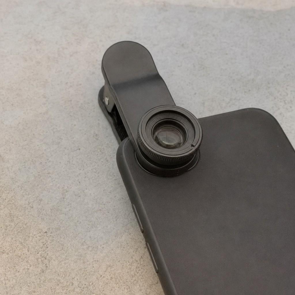 A small clip-on macro lens attached to the back of a phone resting on a plain surface