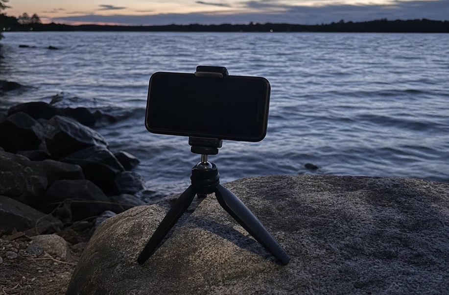 A phone on a small tripod mount by a lakeshore after sunset in blue evening light