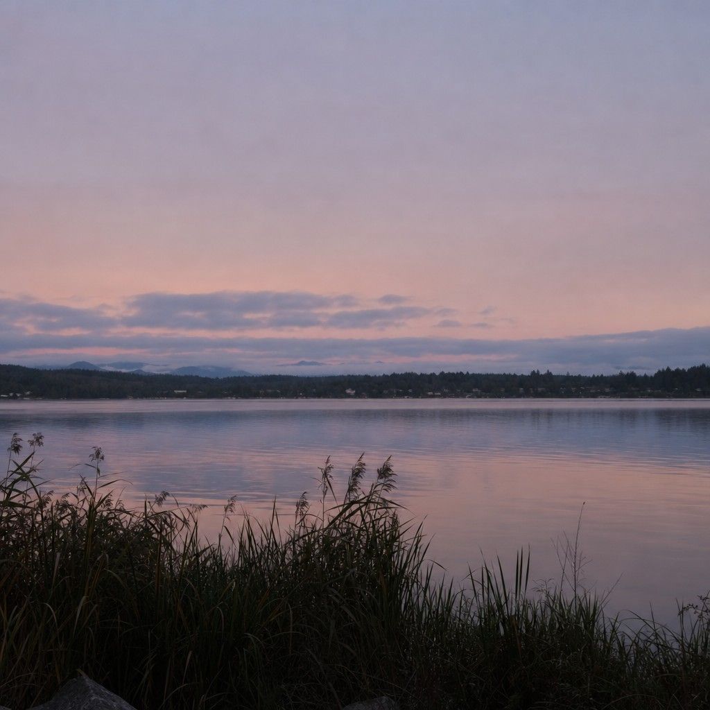 Soft pastel sky over a quiet lake a few minutes before the sun appears, reeds in the foreground