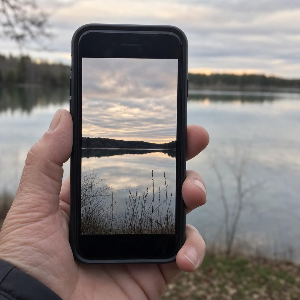 Close view of a smartphone held up against the dawn sky, the screen showing the same scene being framed