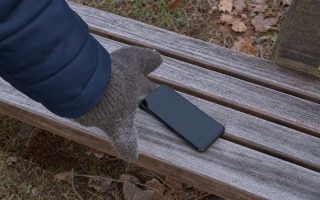 A smartphone lying on a frost covered bench with a gloved hand reaching for it