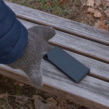 A smartphone lying on a frost covered bench with a gloved hand reaching for it