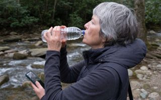 Side close view of an older walker drinking from a water bottle on a trail rest stop near a creek