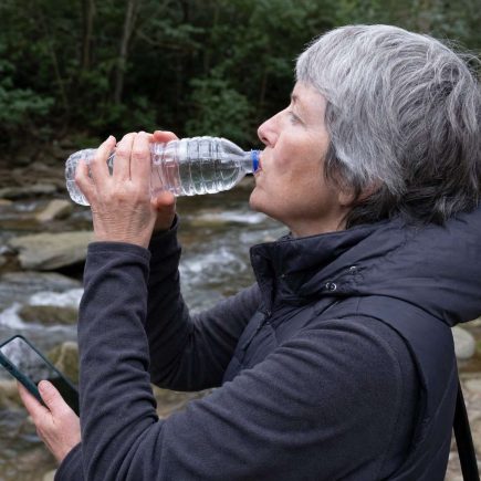 Side close view of an older walker drinking from a water bottle on a trail rest stop near a creek