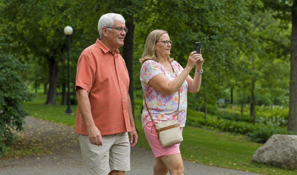 Side view of two people walking together through a park, one carrying a phone ready to shoot