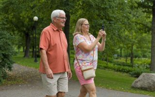 Side view of two people walking together through a park, one carrying a phone ready to shoot
