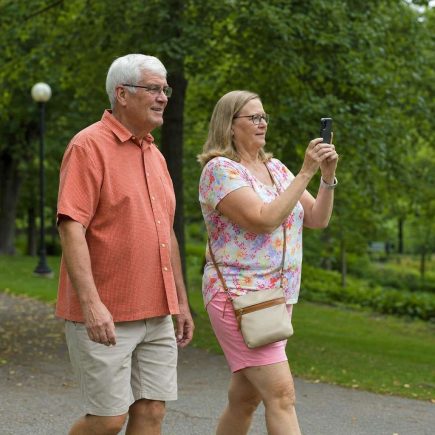 Side view of two people walking together through a park, one carrying a phone ready to shoot