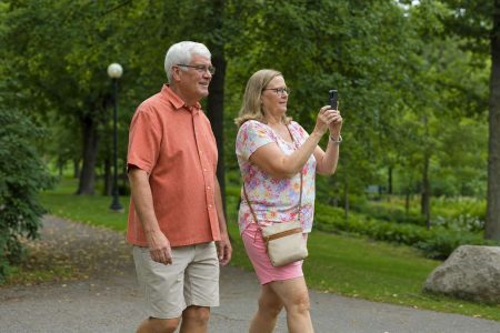 Side view of two people walking together through a park, one carrying a phone ready to shoot