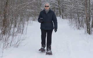 Front wide view of a beginner snowshoeing slowly along a flat snowy trail in winter layers