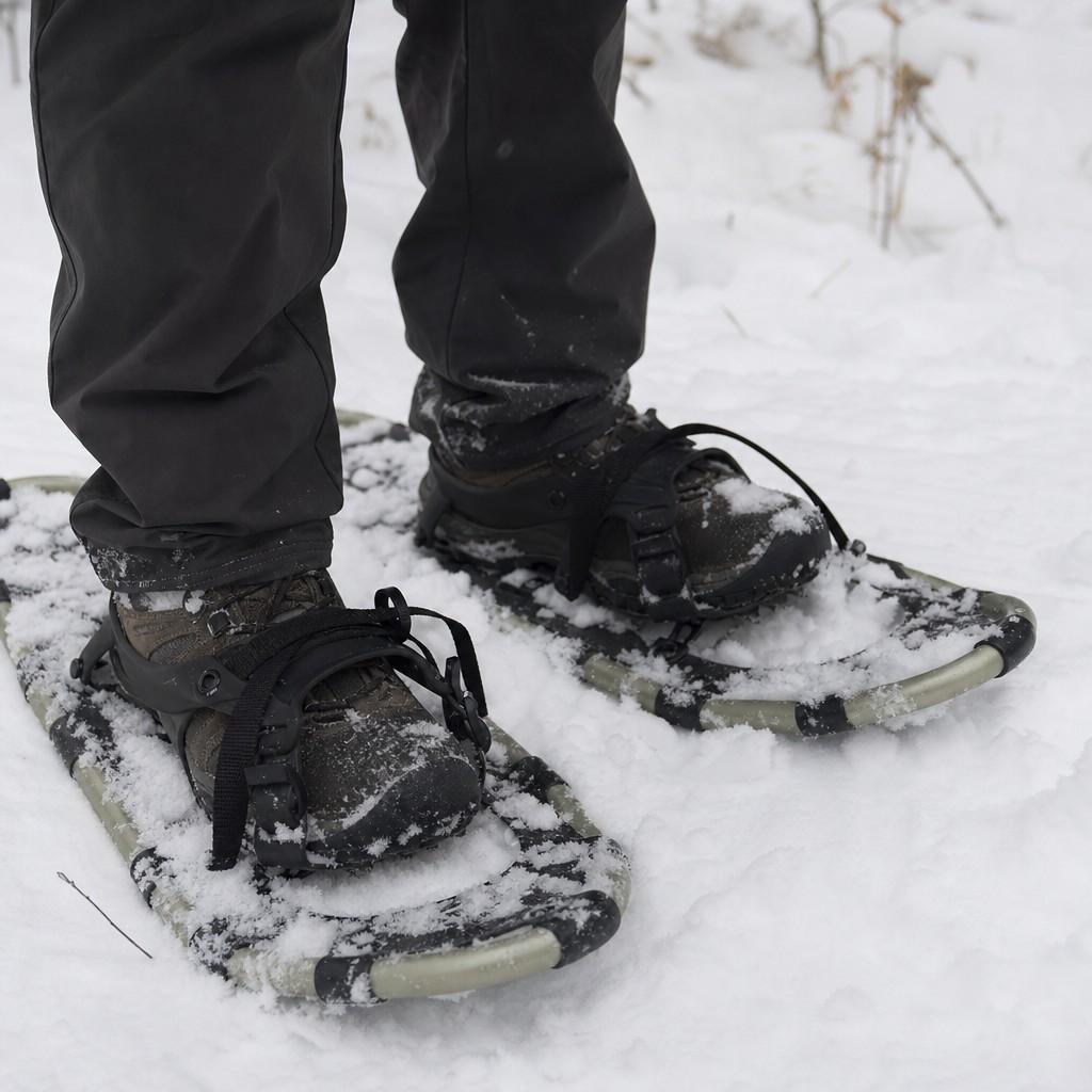 Close view of simple snowshoes strapped to winter boots in fresh snow